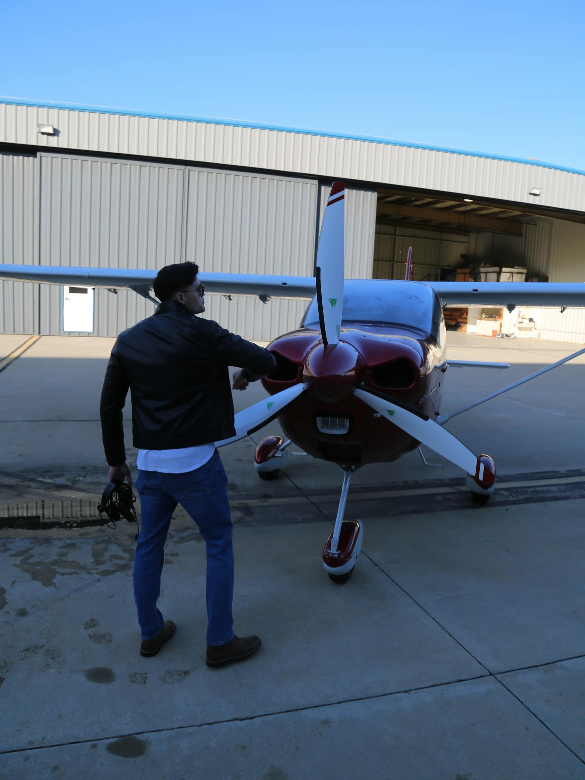 A pilot checking the propeller of a small airplane on the apron in front of a hangar